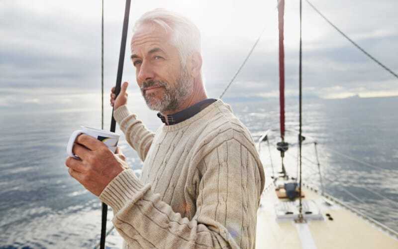 Man on sailboat looking into the distance holding coffee cup